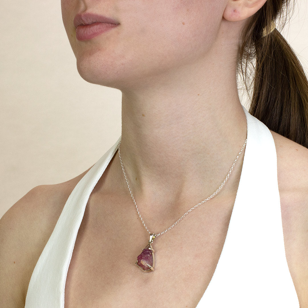 Woman wearing a silver necklace with a pink stone on a plain background