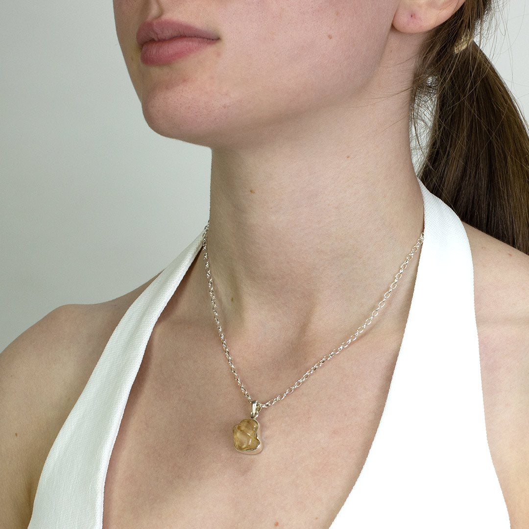 Person wearing a silver necklace with a freeform gemstone on a plain background