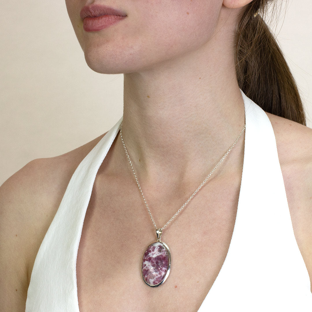 Woman wearing a silver necklace with a pink and white stone pendant on a plain background