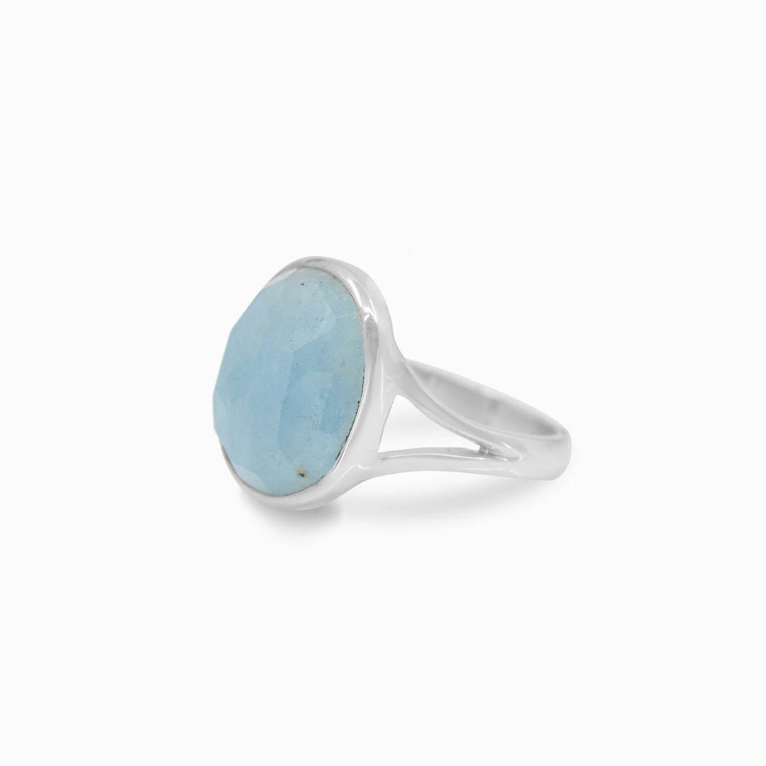 Close-up of a hand wearing a silver ring with a light blue gemstone on a plain background
