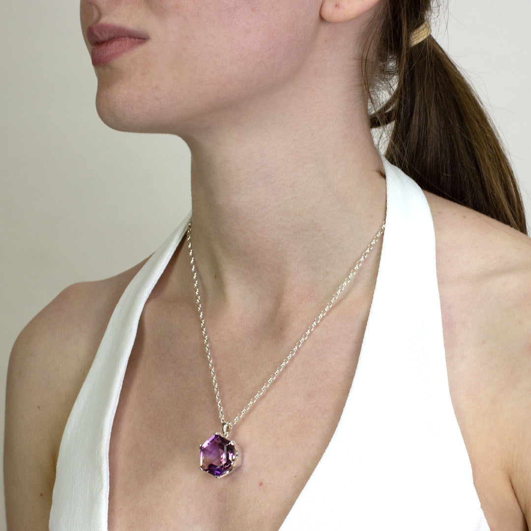 Woman wearing a silver necklace with a hexagonal purple and yellow stone against a plain background
