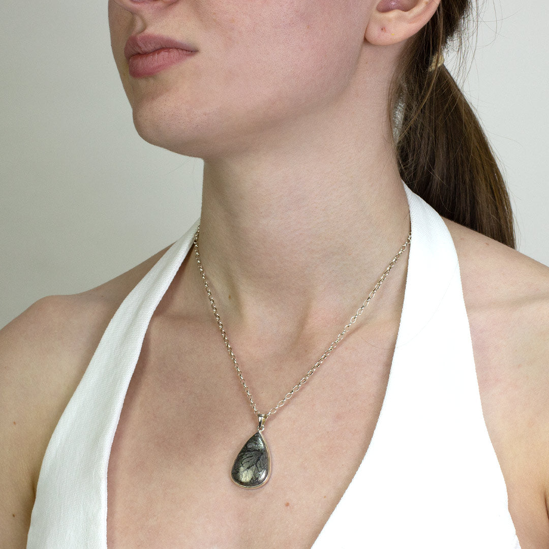 Woman wearing a silver necklace with a metallic stone on a plain background.