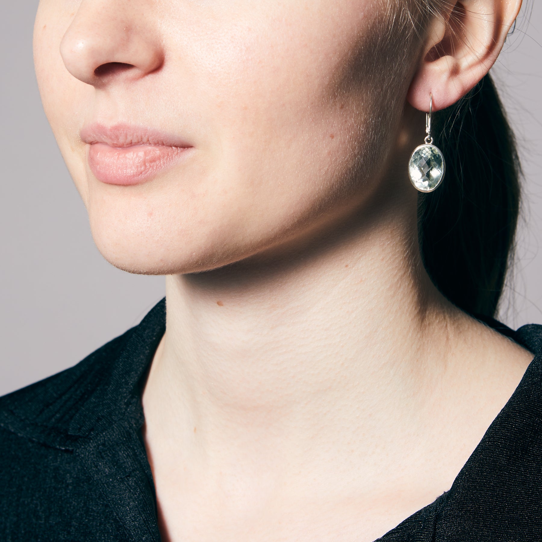 Close-up of a person wearing an earring with a green gemstone on a neutral background