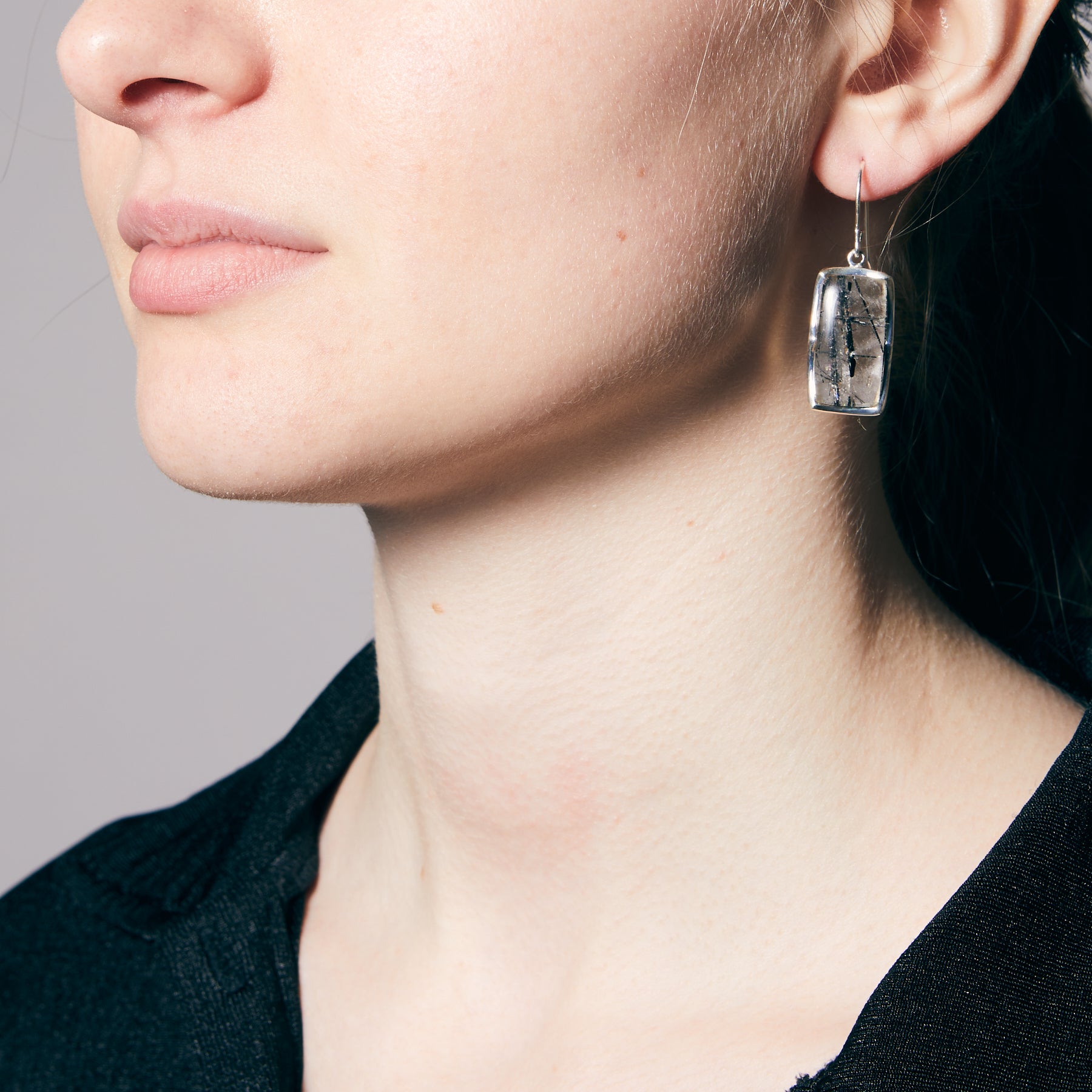 Close-up of a person wearing a clear crystal earring against a neutral background