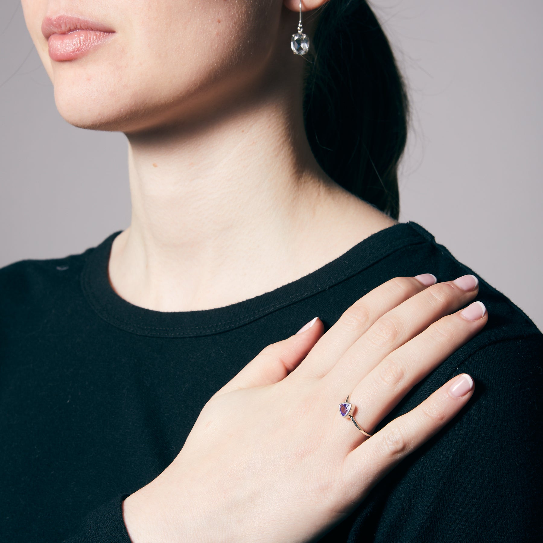 Woman wearing a black top with a hand on her chest, showing a silver ring with a blue gemstone.