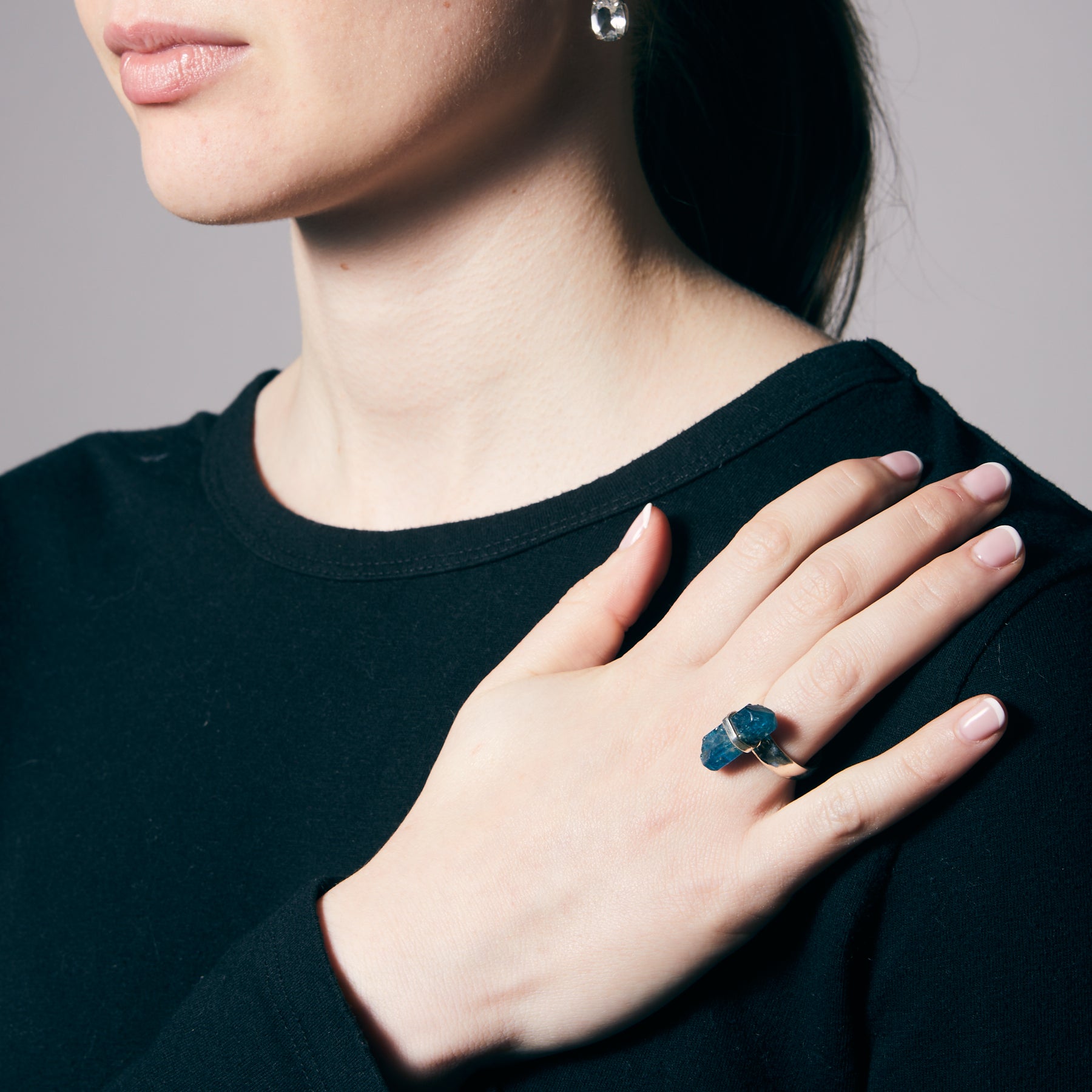 Woman wearing a silver ring with a blue gemstone on a plain background