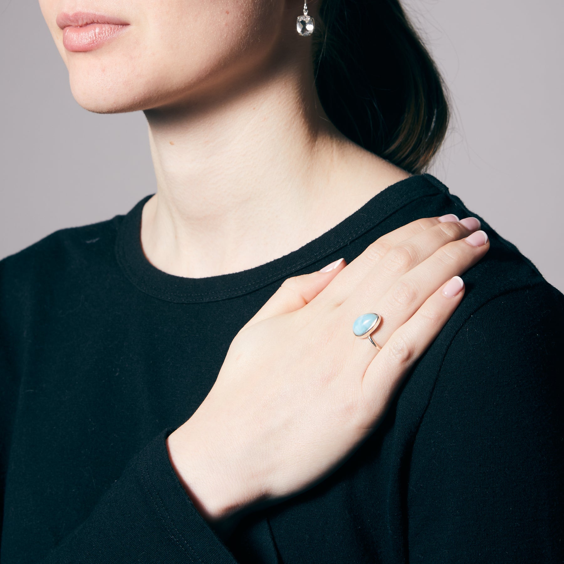Person wearing a black top with a hand resting on their shoulder, showing a ring with a blue gemstone.