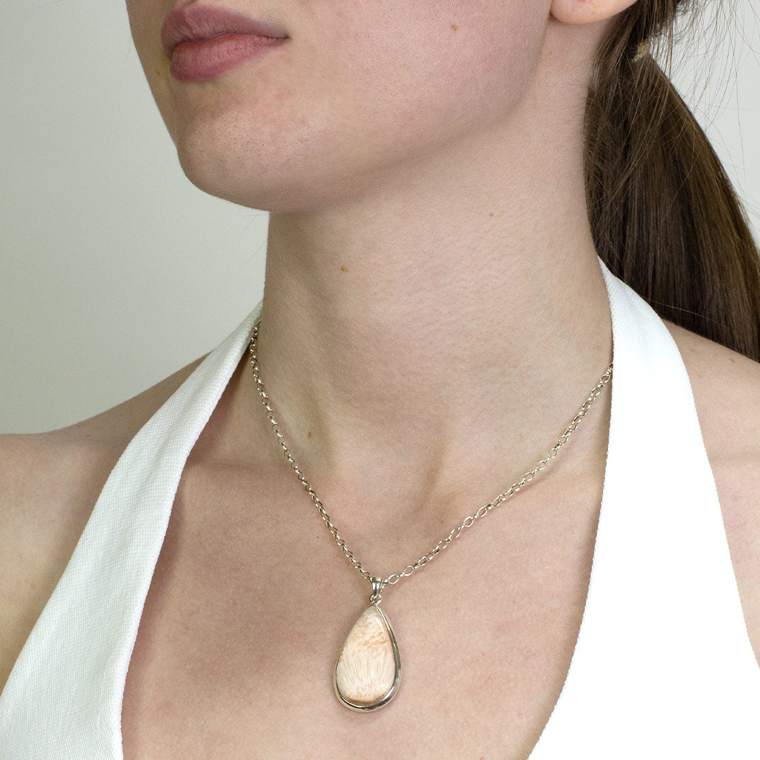 Woman wearing a silver necklace with a light pink gemstone on a plain background.