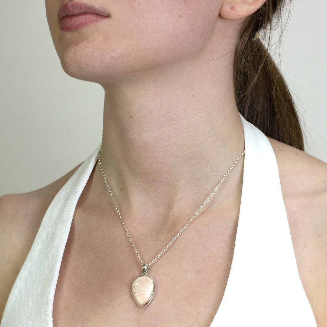 Woman wearing a silver necklace with a light pink gemstone on a plain background.