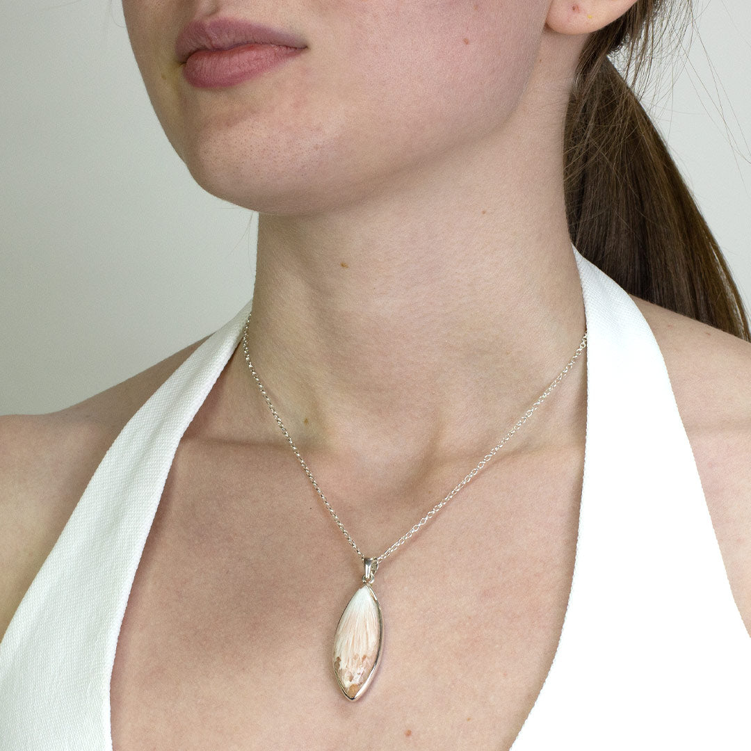 Woman wearing a silver necklace with a light pink gemstone on a plain background.