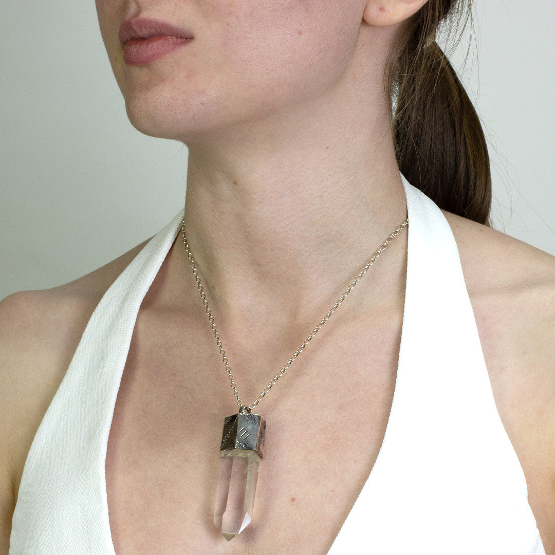 Woman wearing a silver necklace with a clear stone on a plain background