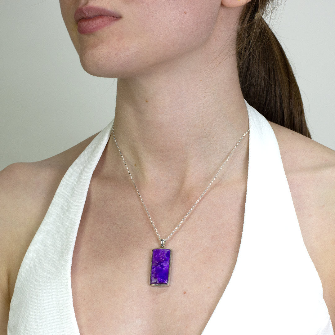Woman wearing a silver necklace with purple gemstone on a plain background.