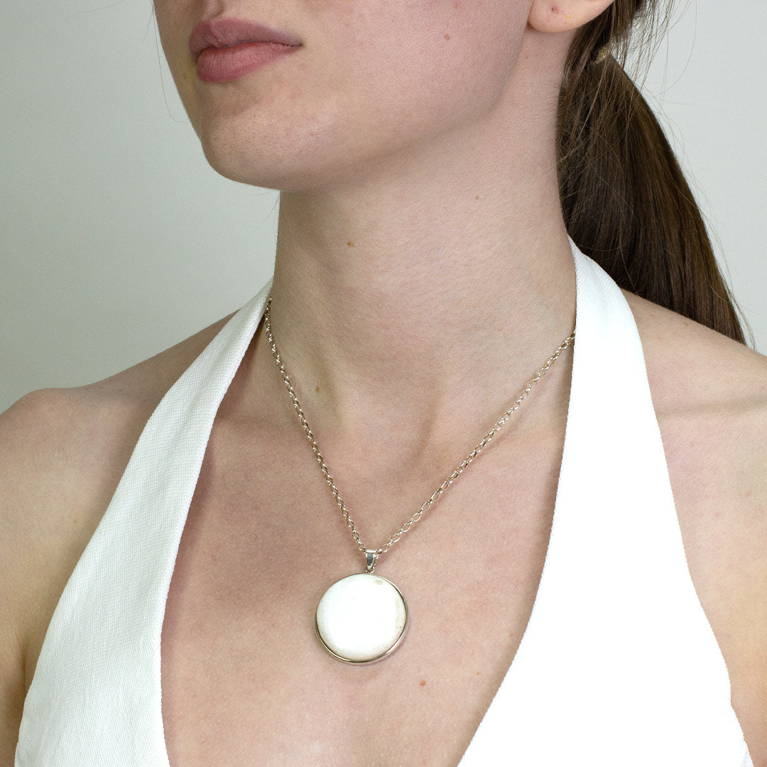 Woman wearing a silver necklace with a white stone pendant on a plain background