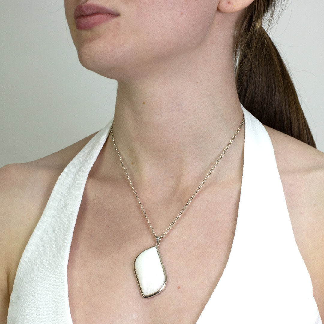 Woman wearing a silver necklace with a white stone pendant on a plain background