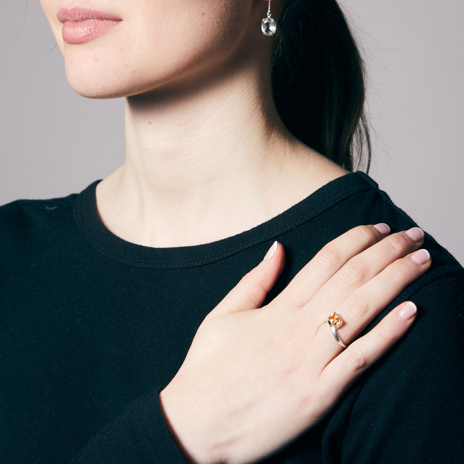 Close-up of a person wearing a black top with a hand resting on their shoulder, featuring a citrine ring.