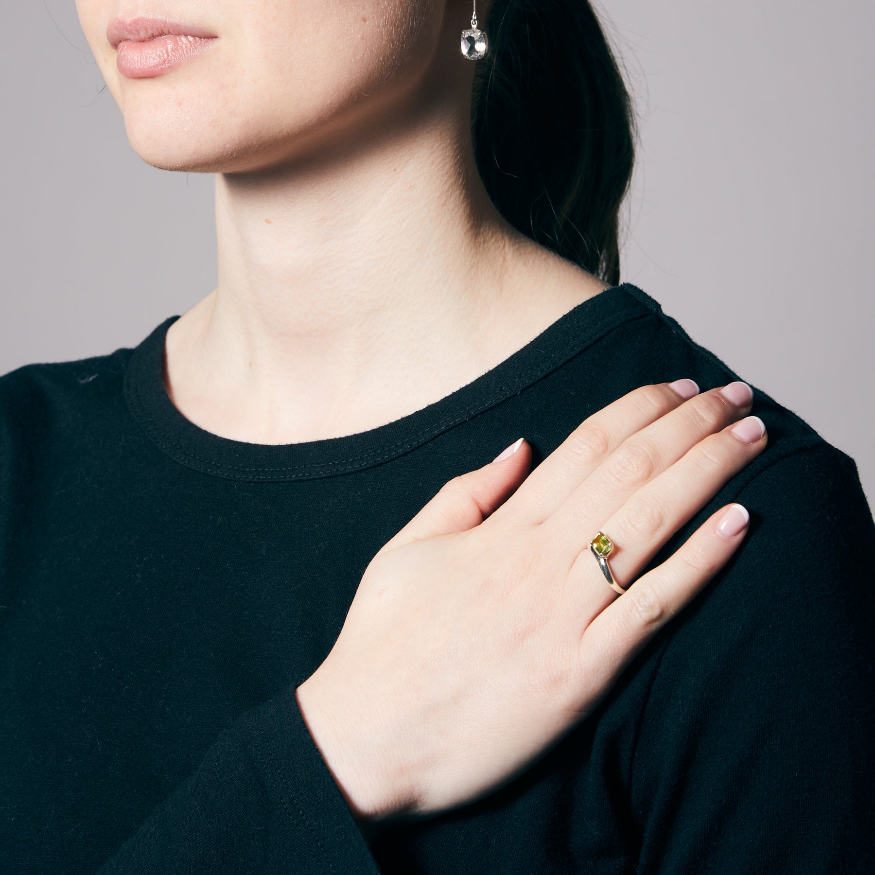 Close-up of a person wearing a ring with a green gemstone on a neutral background