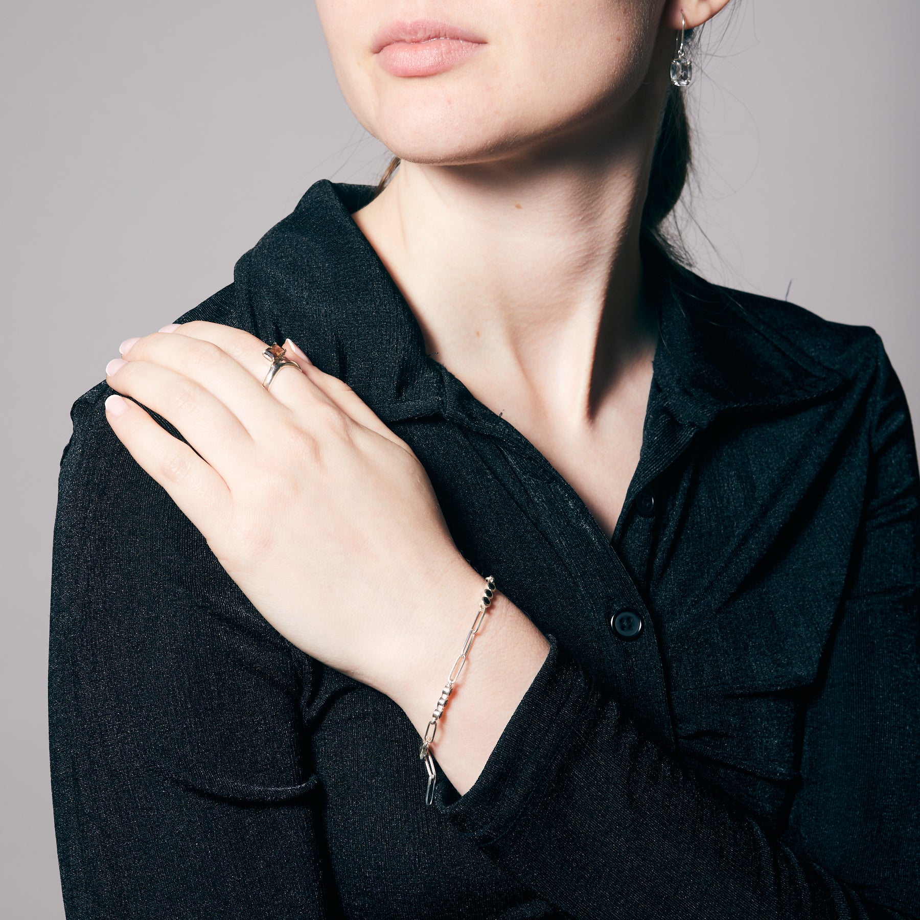 Person wearing a black shirt with a focus on jewelry including a ring and a bracelet with black gemstones.
