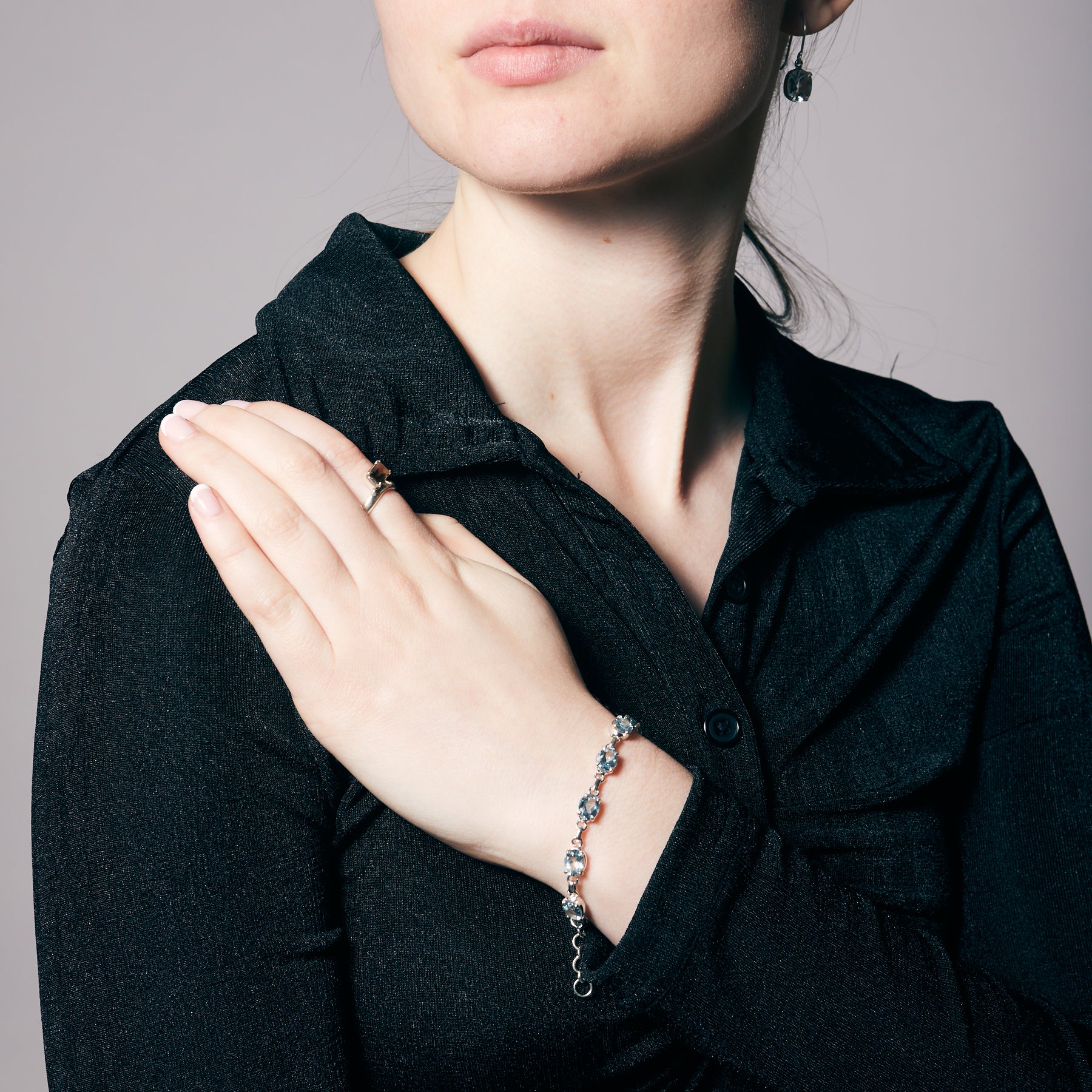 Person wearing a black shirt with a bracelet with light blue gemstones on a neutral background.