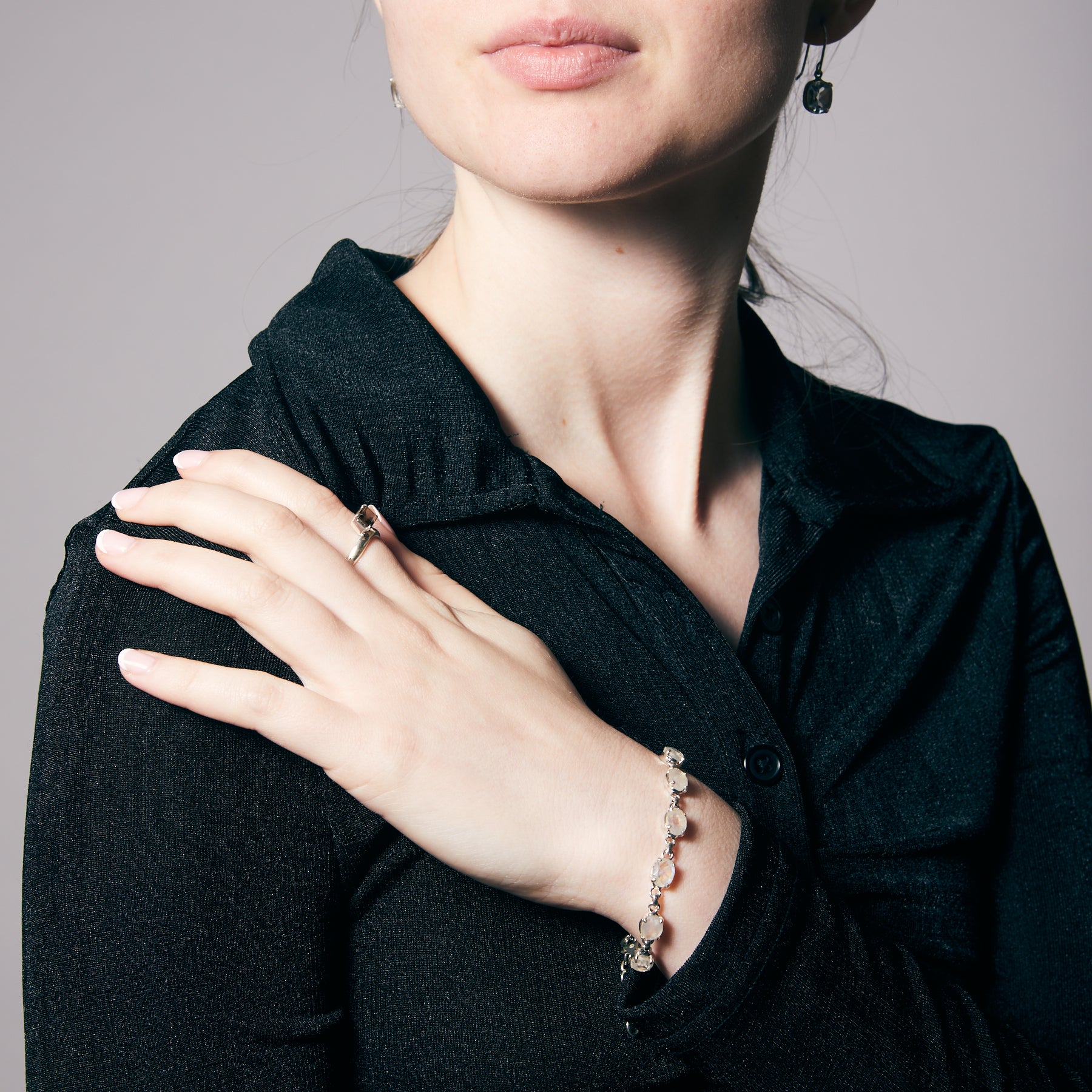 Woman wearing a ring and a moonstone bracelet on a neutral background