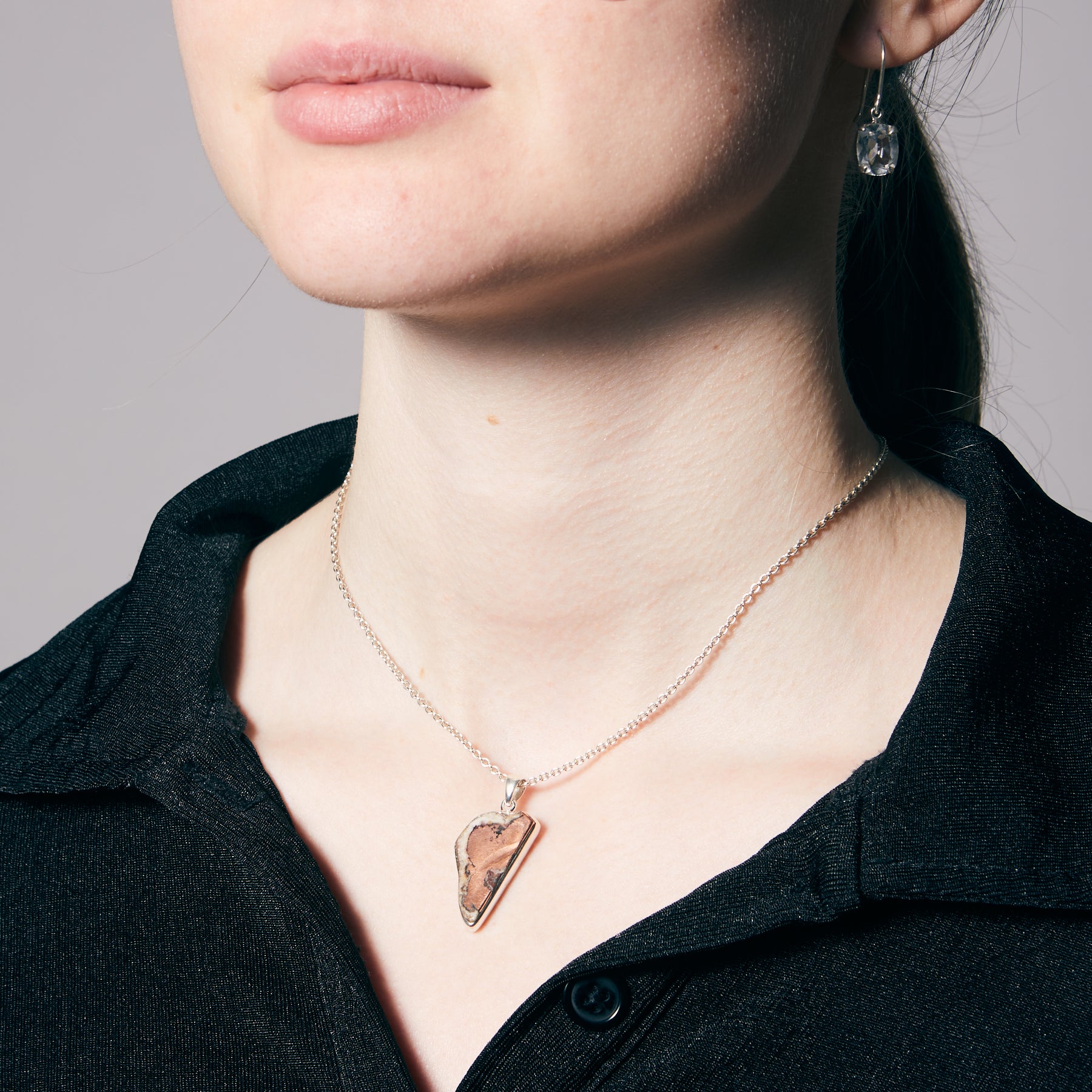 Person wearing a necklace with a metallic pendant against a neutral background