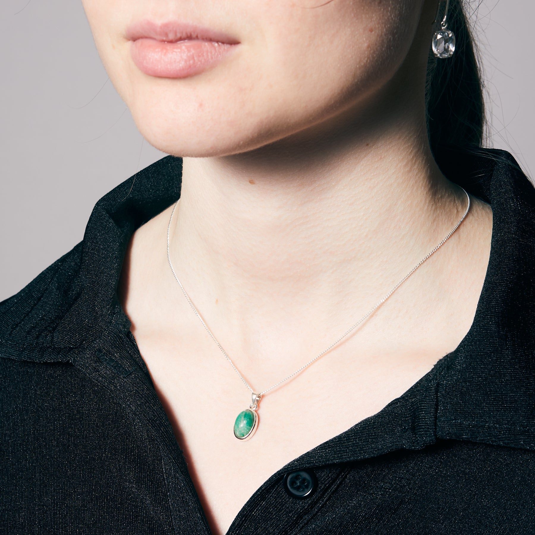 Person wearing a black shirt with a green pendant necklace and clear earring.