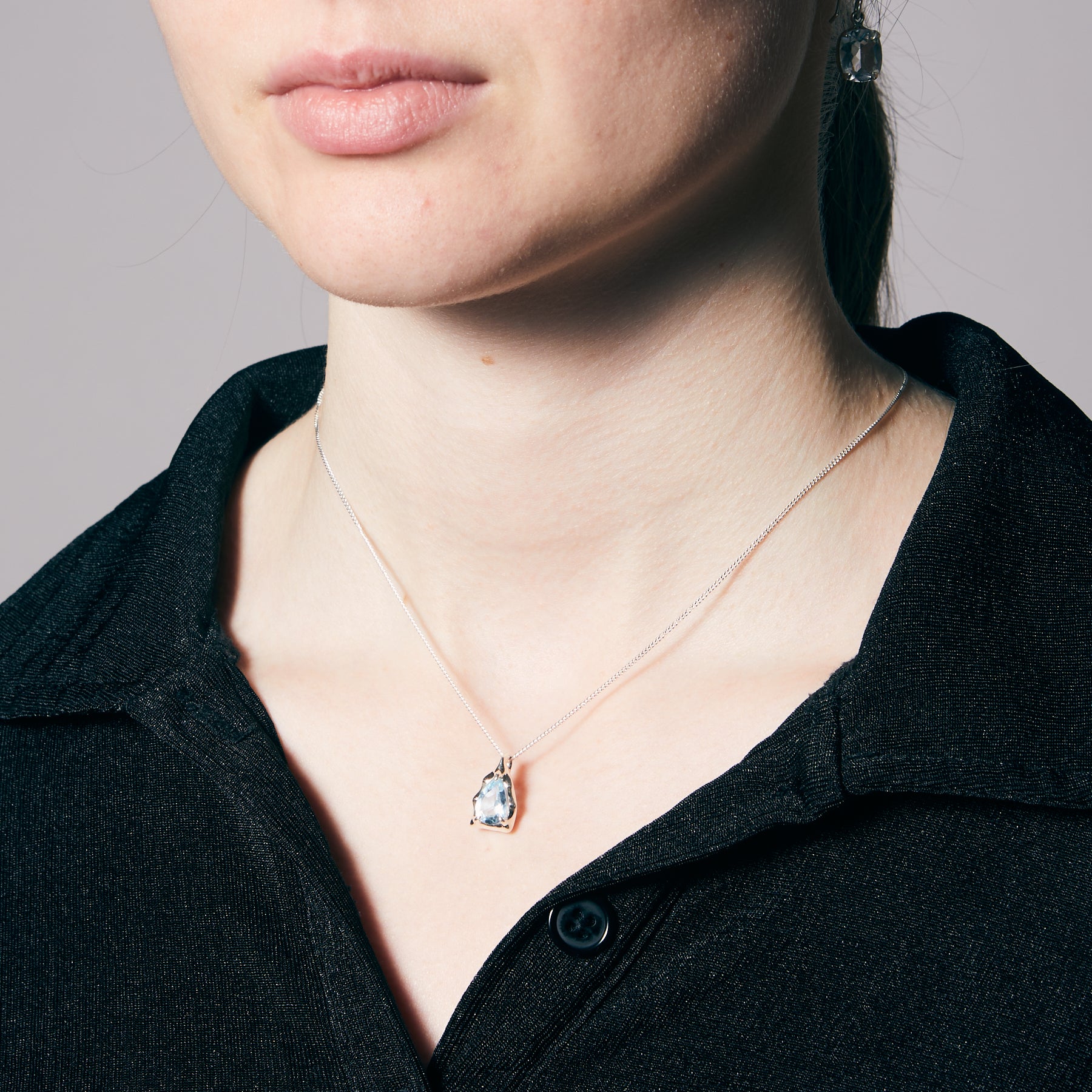 Necklace with a blue stone pendant worn by a person against a neutral background