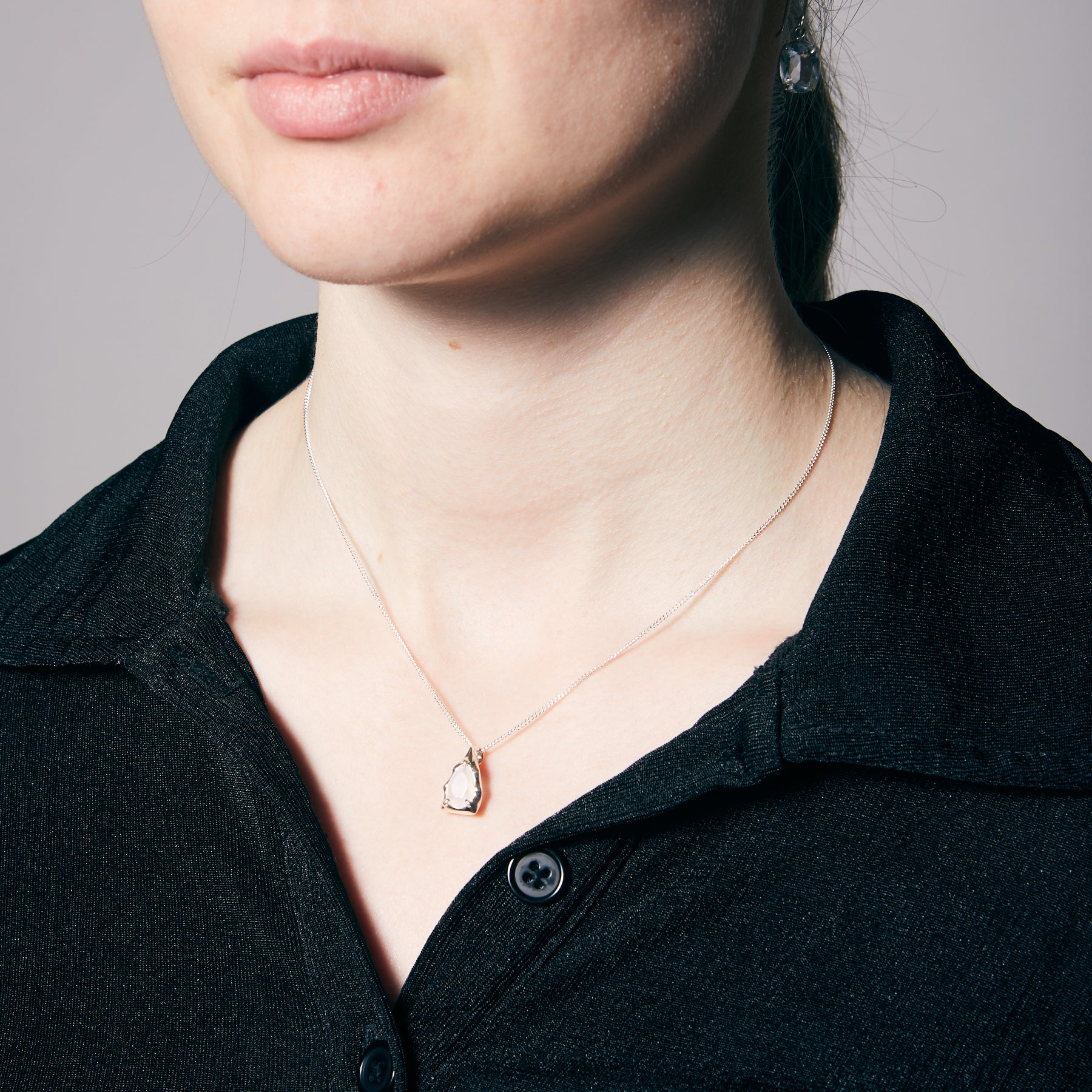 Person wearing a delicate necklace with a moonstone pendant against a neutral background
