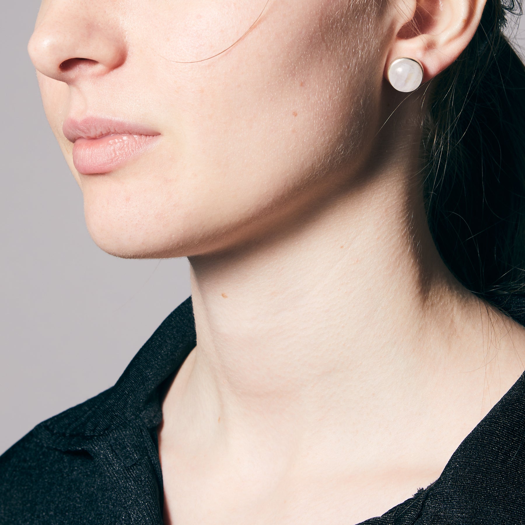 Close-up of a person wearing moonstone earrings with a neutral background