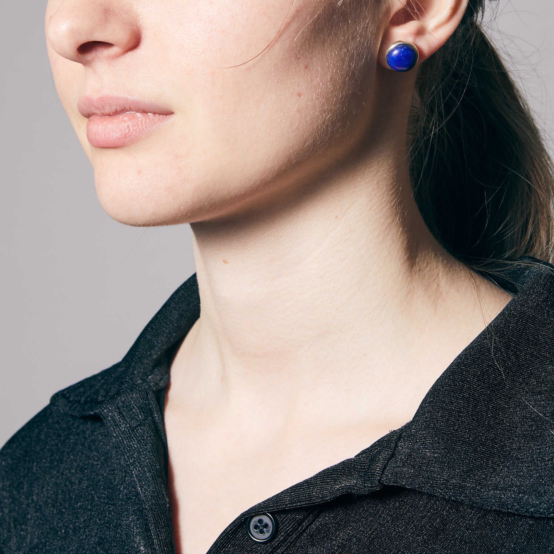 Close-up of a person wearing blue earrings on a neutral background