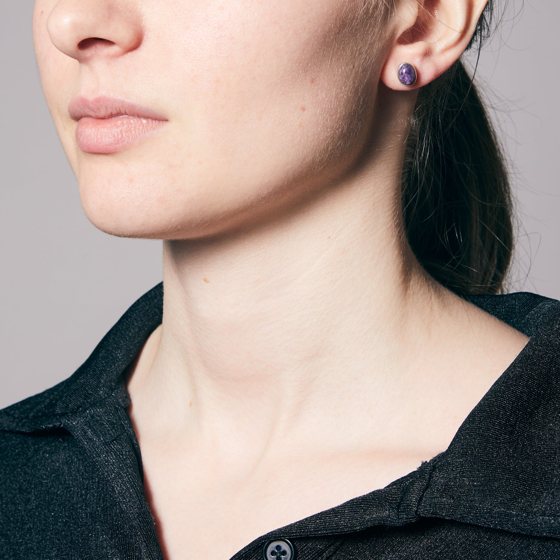 Person wearing purple stud earrings on a neutral background.