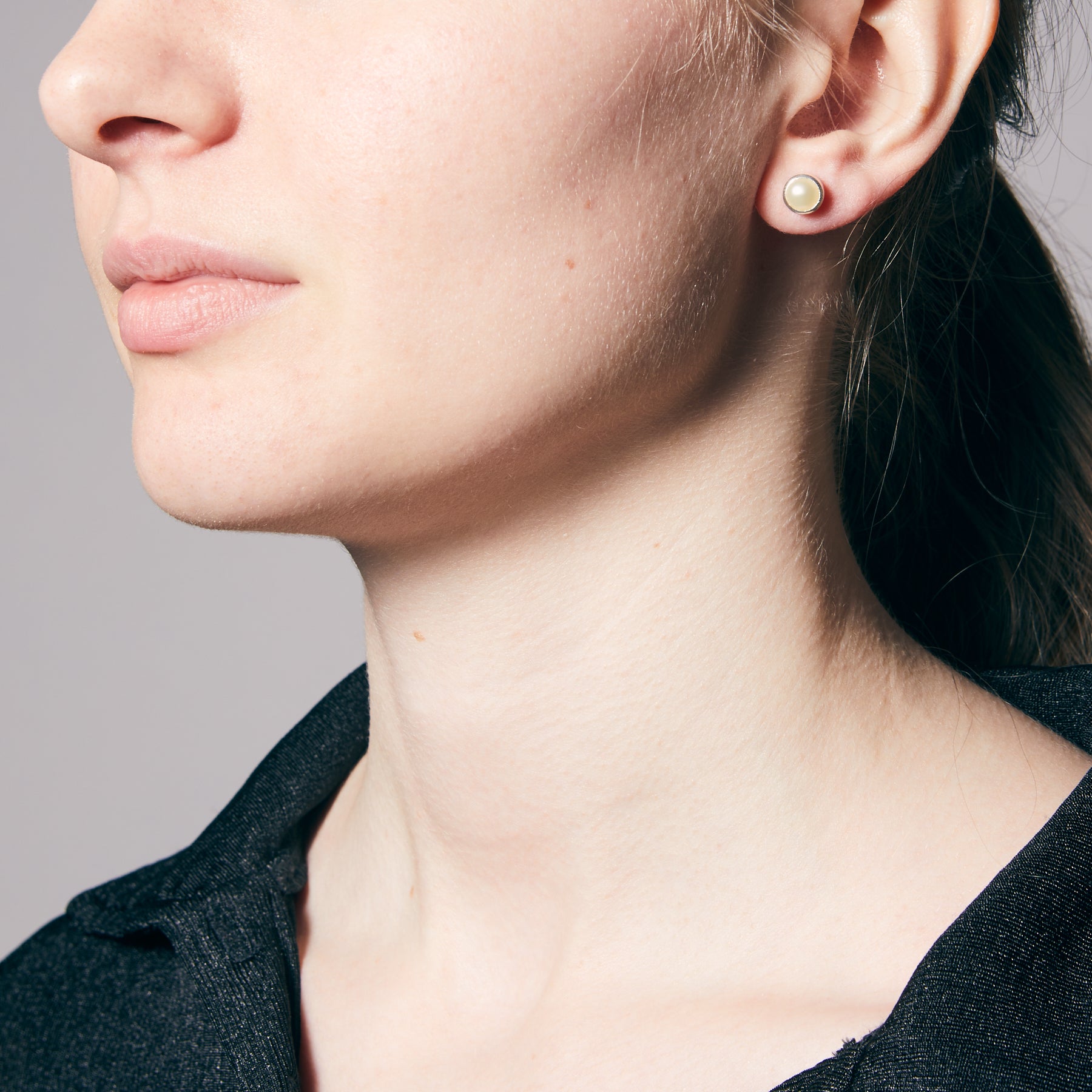 Close-up of a person wearing pearl earrings against a neutral background