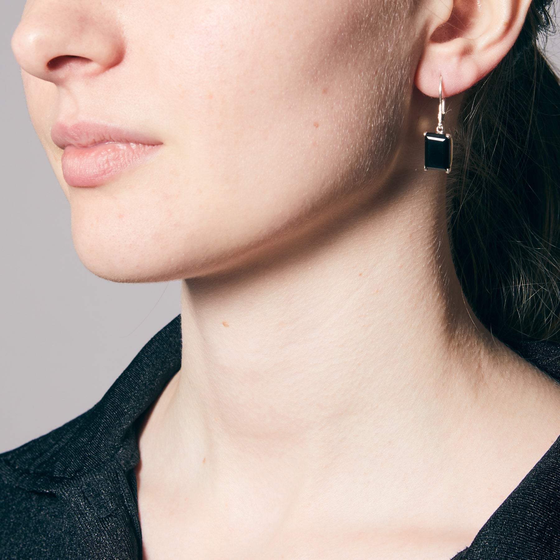 Close-up of a person wearing a black earring against a neutral background