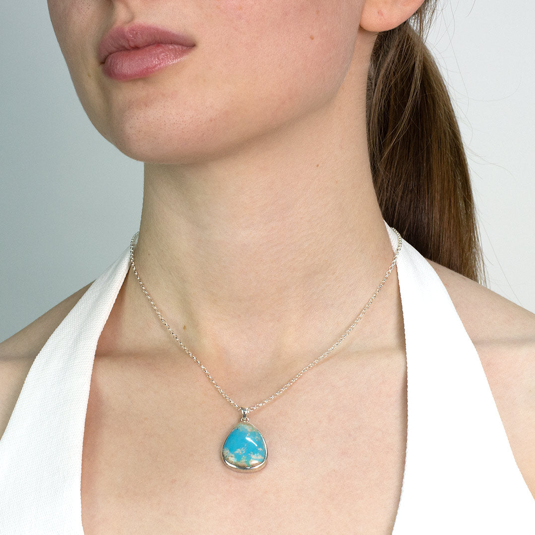 Woman wearing a necklace with a turquoise pendant against a neutral background