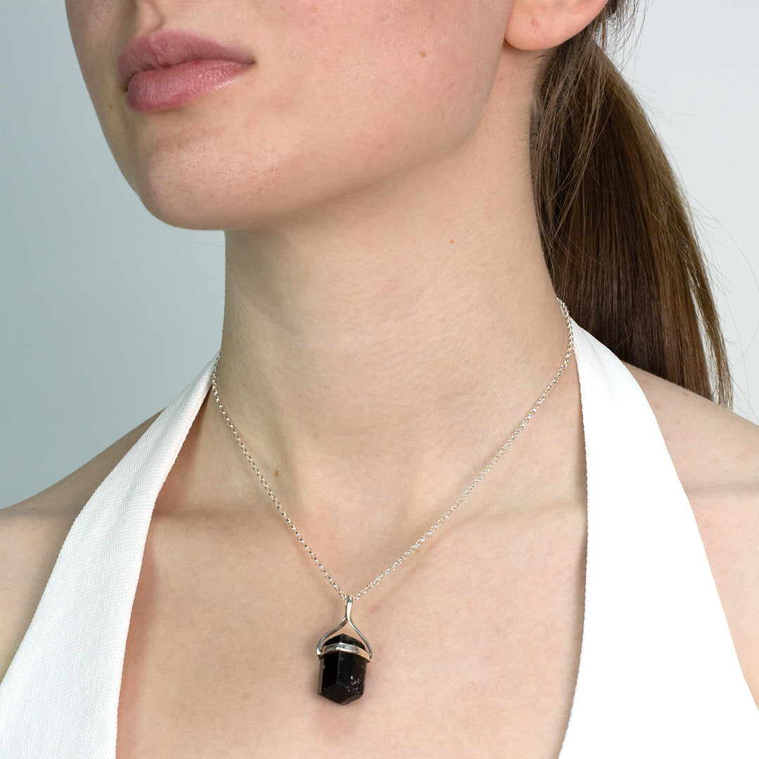 Woman wearing a necklace with a black pendant against a neutral background