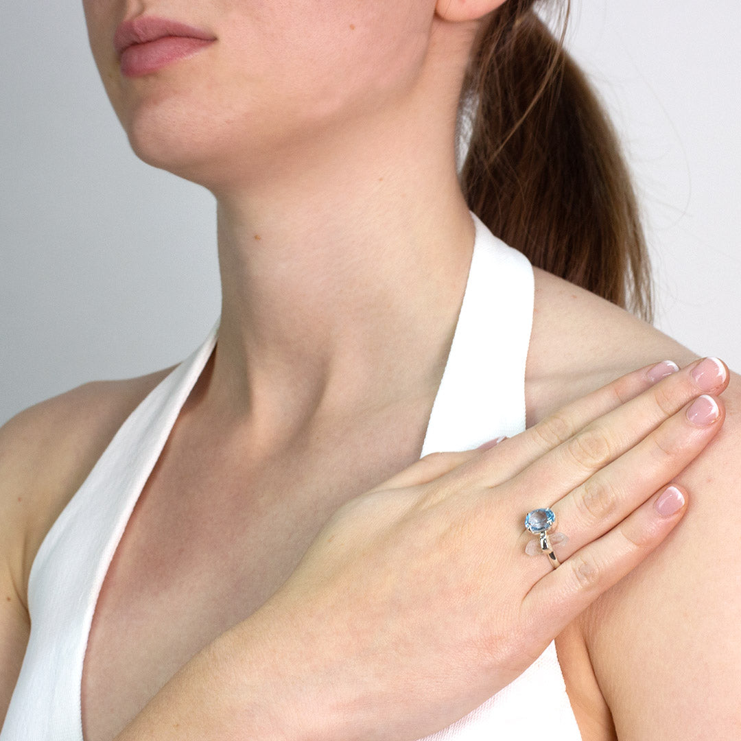 Woman wearing a silver ring with blue and clear gemstones against a plain background