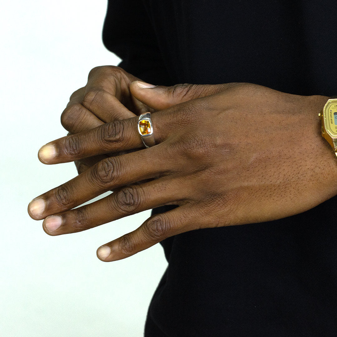 Close-up of a hand wearing a silver ring with a yellow gemstone on a white background