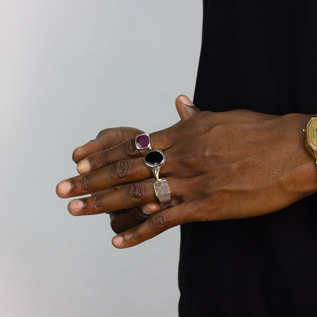 Hand wearing multiple silver rings against a plain background