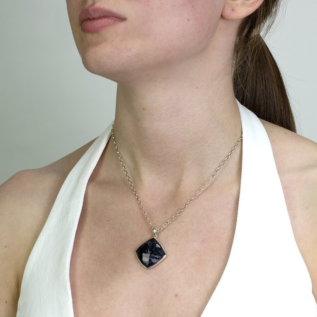 Woman wearing a silver necklace with a dark blue stone on a plain background