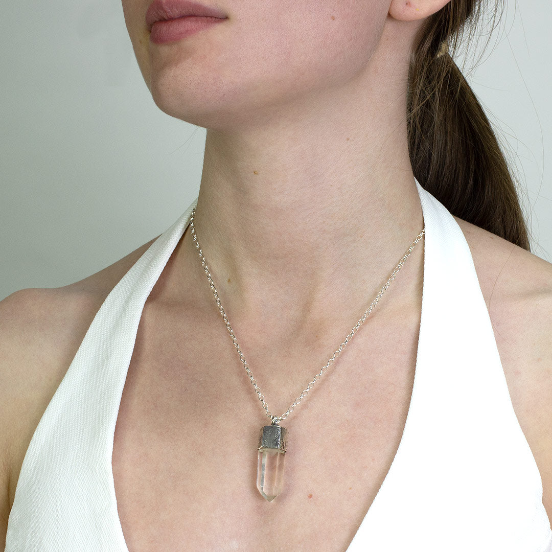 Woman wearing a silver necklace with a clear stone on a plain background.
