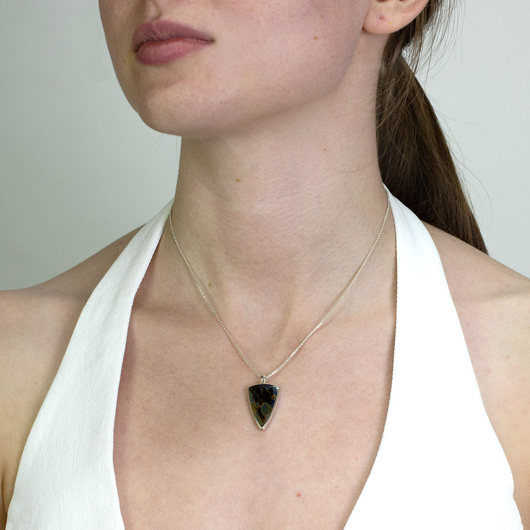 Woman wearing a silver necklace with a stone with dark blue patterns on a plain background