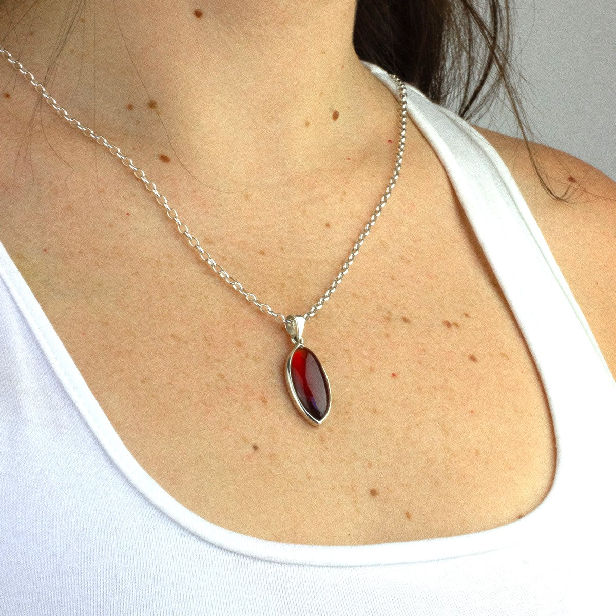 Close-up of a woman wearing a silver pendant necklace featuring an orange gemstone on a plain background.