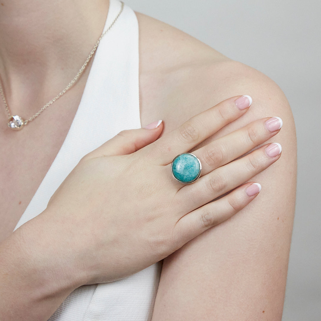Close-up of a hand wearing a silver ring with a green gemstone on a plain background