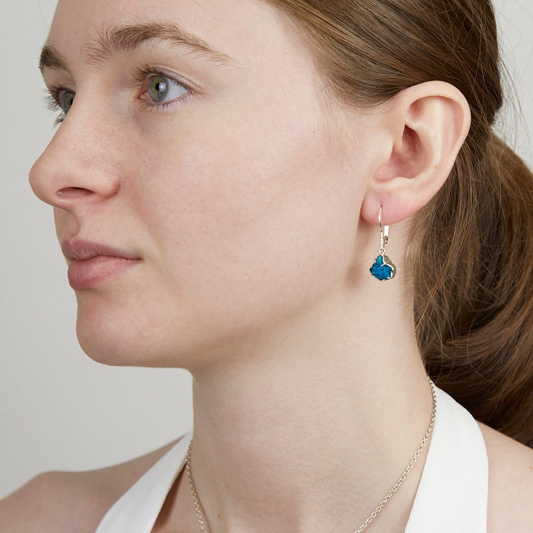 Close-up of a woman wearing a silver earring with blue gemstone on a plain background