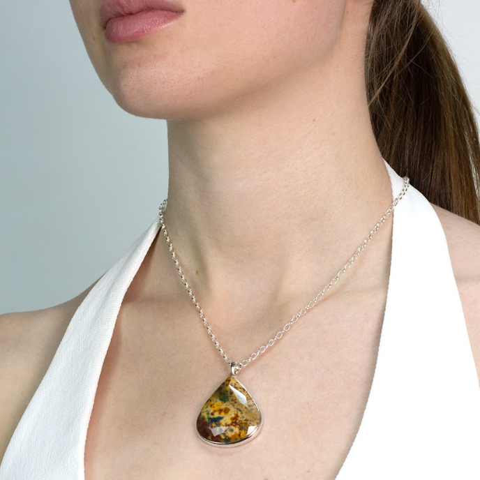 Woman wearing a teardrop-shaped pendant with a brown, green and yellow pattern on a plain background