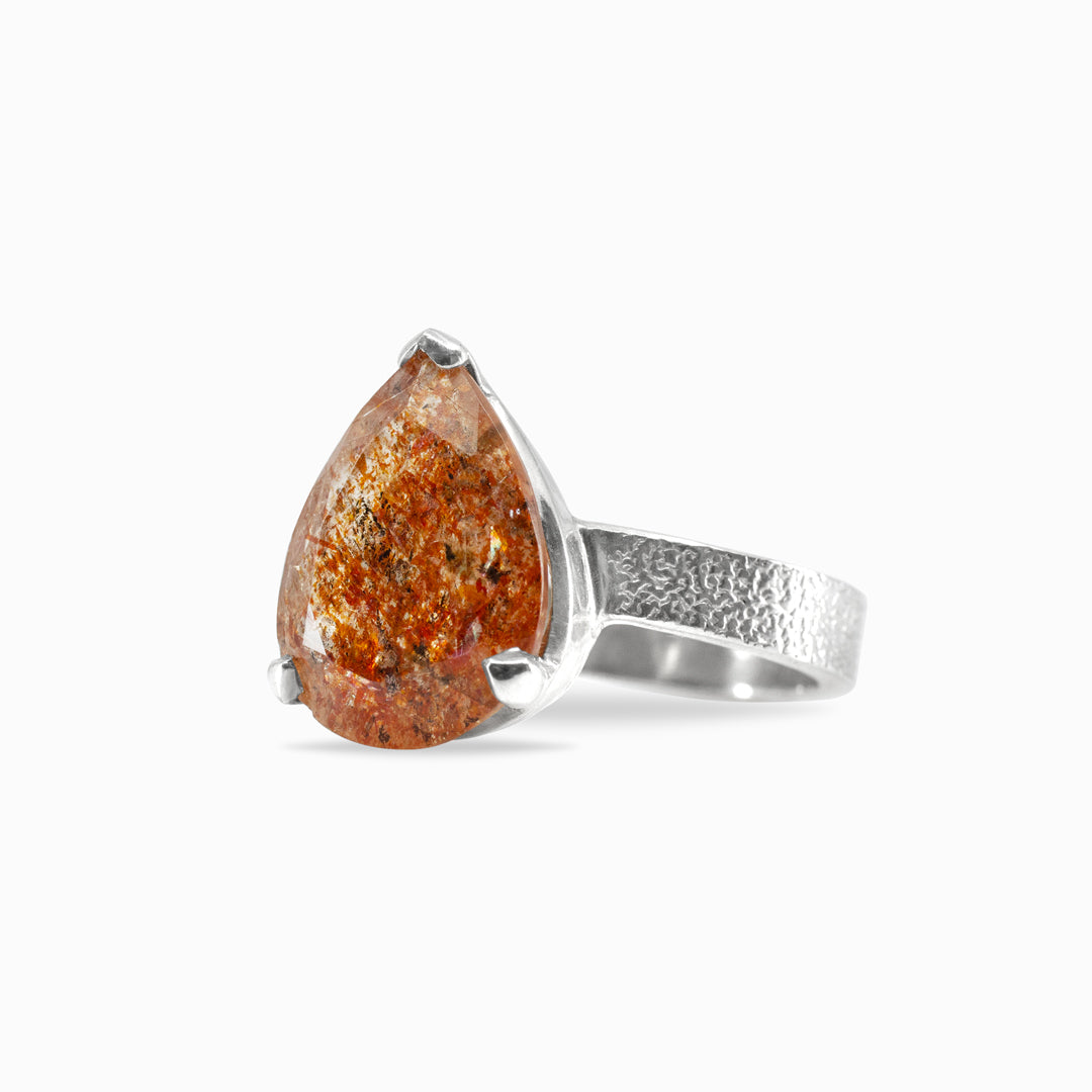 Silver ring with a teardrop-shaped orange gemstone on a white background