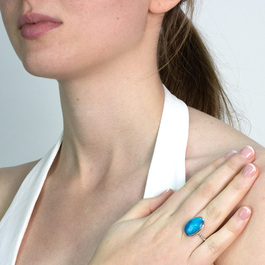 Woman wearing a silver ring with a blue gemstone on a plain background
