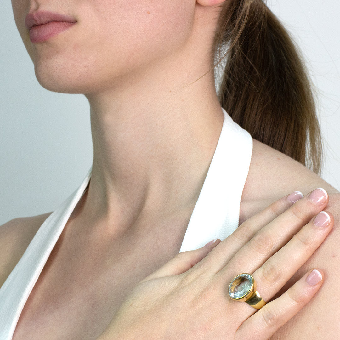 Close-up of a woman wearing a golden ring with a light blue gemstone on a plain background.