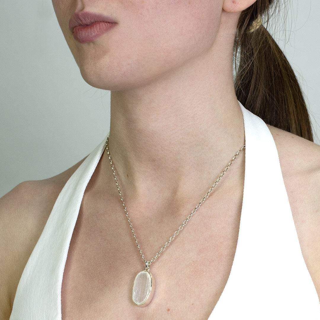 Woman wearing a silver necklace with a white stone pendant on a plain background