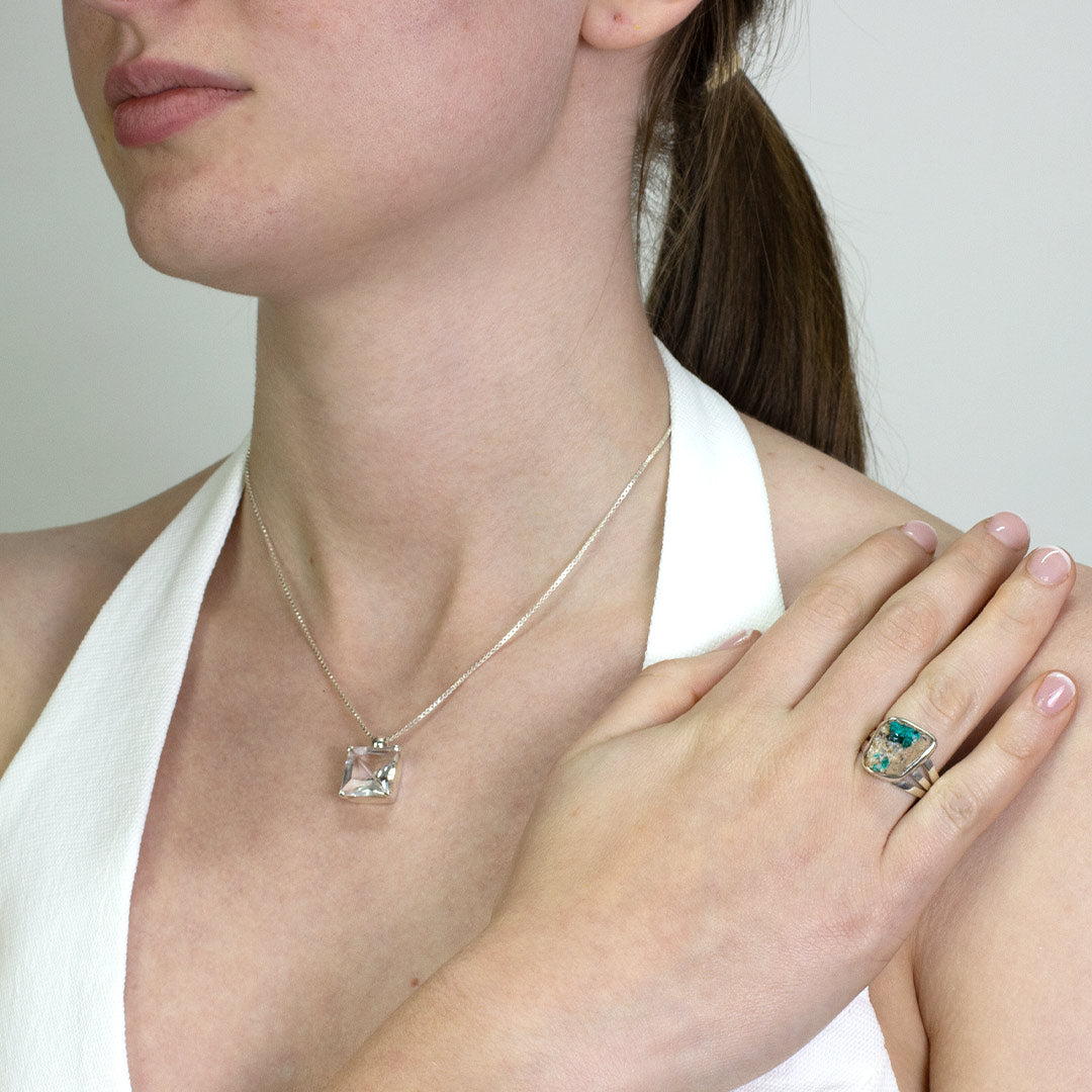 Woman wearing a silver ring with a rough freeform green gemstone on a plain background