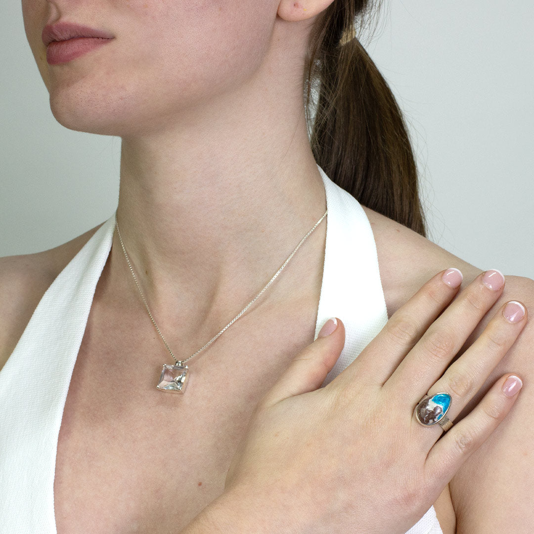Woman wearing a silver ring with a teardrop shaped blue and brown stone on a plain background